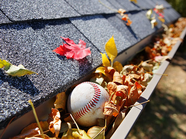 Rain gutters full of autumn leaves with a baseball